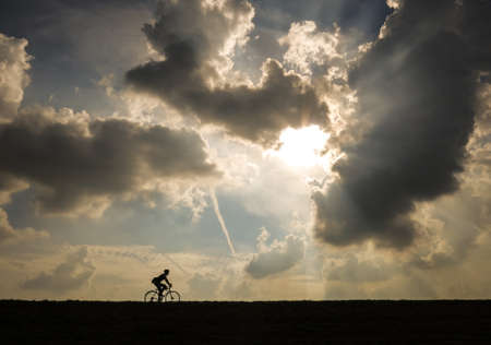 a man riding his bike in front of a dramatic skyの写真素材