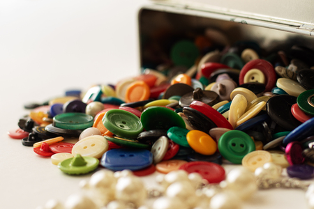 From the upturned white box with painted flowers, multi-colored buttons for clothes rolled out. In the foreground is a blurred pearl.の写真素材