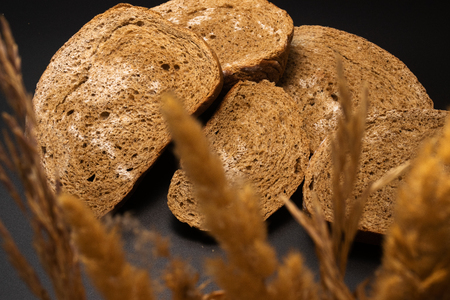 Several slices of rye bread, covered with mold, are located on a table in a heap together with dry spikelets. Photo at a slight angle on a black background.の写真素材