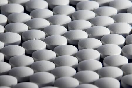 A large number of white tablets in rows lie on the table. They fill the whole photo. Photo taken at...