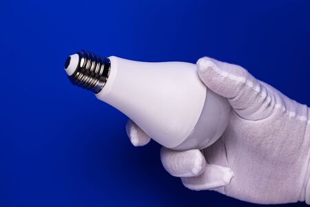A man's hand in a white cotton glove holds the LED light bulb with a plinth up.の写真素材