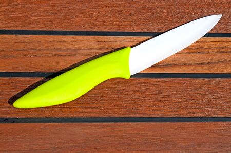 A ceramic knife with a white blade and a green grip on a wooden cutting board の写真素材