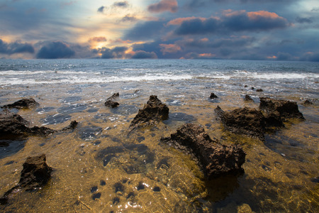 receding sea coastline and stone with water pits at sunsetの写真素材