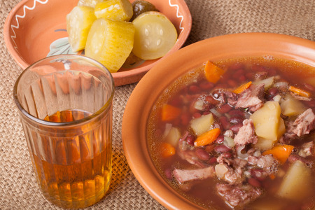 Soup with bean and potato, salty cucumbers and moonshine on a sackclothの写真素材