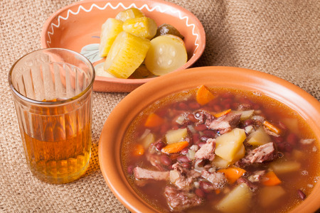 Soup with bean and potato, salty cucumbers and moonshine on a sackclothの写真素材