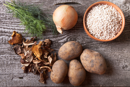 Dried mashrooms, potato, onion, dill and grain in a bowl on a old wooden boardの写真素材
