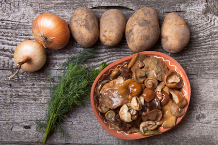 Salty mashrooms, potato, onion, dill and grain in a bowl on a old wooden boardの写真素材