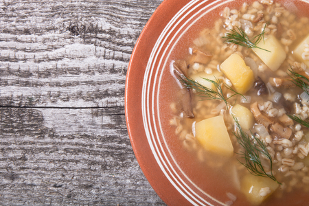 Soup with grits, mushrooms, potatoes and dill in a bowl on old wooden boardの写真素材