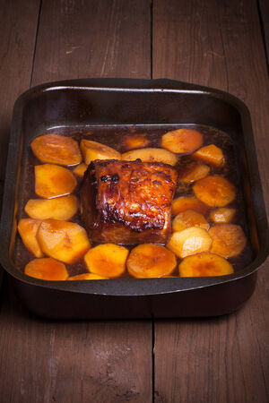 piece of pork and potatoes in the pan for roasting on an old wooden tableの写真素材