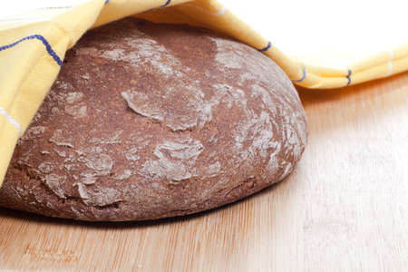 Rye bread under a towel on a wooden boardの写真素材