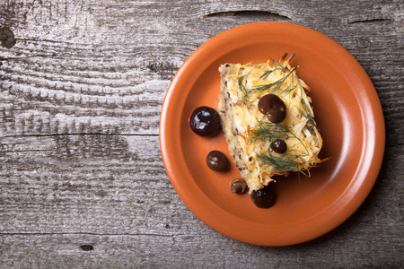 potato casserole with salted mushrooms in a clay plate on old wooden tableの写真素材