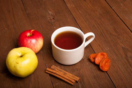 Cup of tea on old wooden table with two apples, dried apricots and cinnamonの写真素材