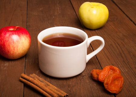 Cup of tea on old wooden table with two apples, dried apricots and cinnamonの写真素材