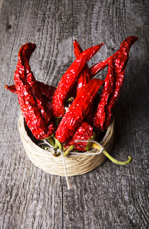 bunch of red hot peppers lying in a wicker basket on old wooden tableの写真素材