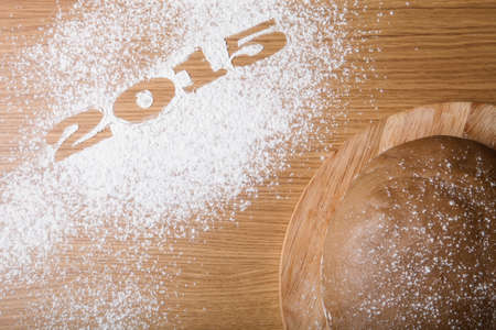 Inscription 2015 on flour and dough on a wooden table