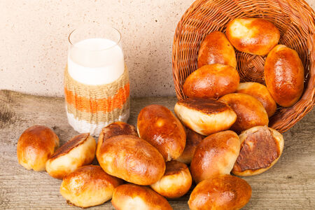 pies with meat or cabbage in a wicker basket and a glass of milk on a wooden background.の写真素材