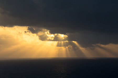 Dramatic sunset rays through a cloudy dark sky over the oceanの写真素材