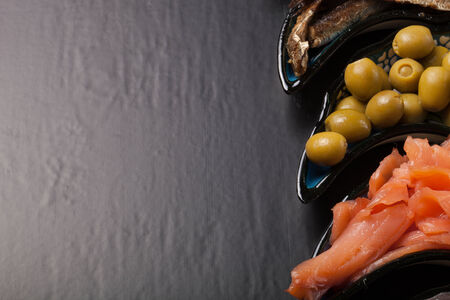 Fish assortment and olives on a plate on a dark background. With space for textの写真素材