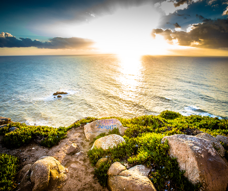 Dramatic sunset rays through a cloudy dark sky over the oceanの写真素材