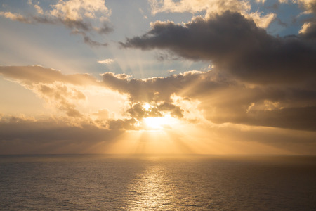 Dramatic sunset rays through a cloudy dark sky over the oceanの写真素材