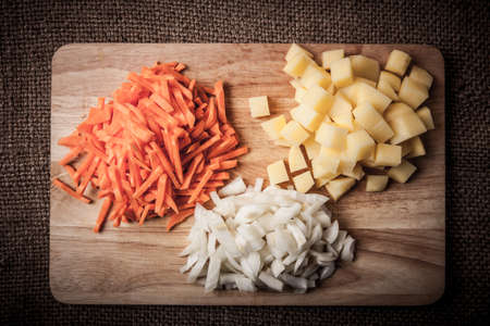 chopped onions, carrots, potatoes stacked in groups on a wooden boardの写真素材
