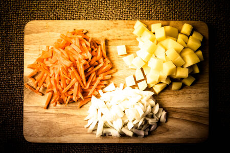 chopped onions, carrots, potatoes stacked in groups on a wooden boardの写真素材