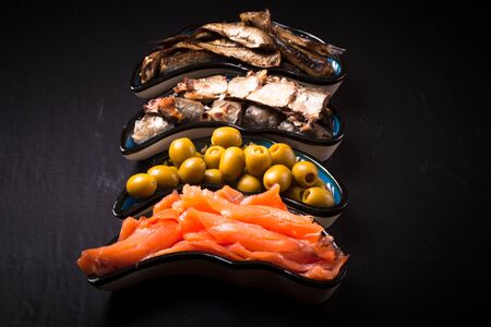 Fish assortment and olives on a plate on a dark background. With space for textの写真素材