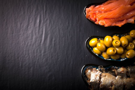 Fish assortment and olives on a plate on a dark background. With space for textの写真素材