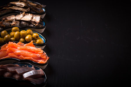 Fish assortment and olives on a plate on a dark background. With space for textの写真素材