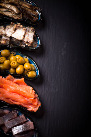 Fish assortment and olives on a plate on a dark background. With space for textの写真素材