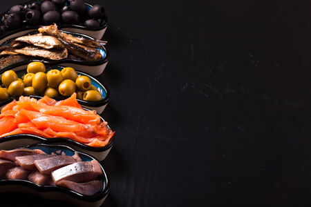 Fish assortment and olives on a plate on a dark background. With space for textの写真素材