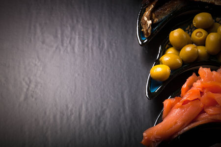 Fish assortment and olives on a plate on a dark background. With space for textの写真素材