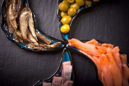 Fish assortment and olives on magic plates on a dark backgroundの写真素材