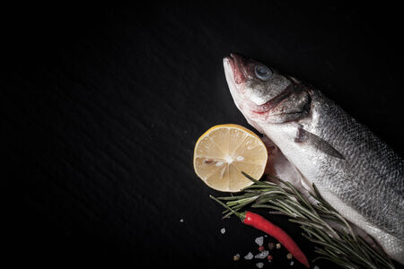 Fresh fish, lemon, pepper and rosemary on a black background. Tintedの写真素材