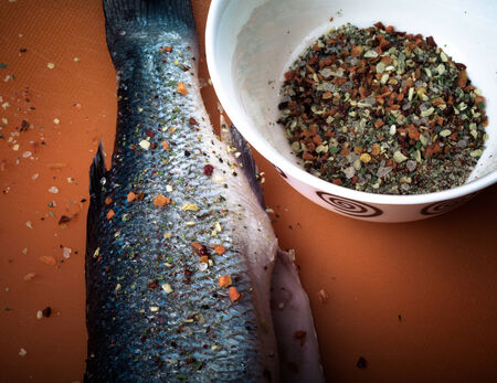fish and spices on a plastic cutting board. Fish in the process of rubbing spices. tintedの写真素材