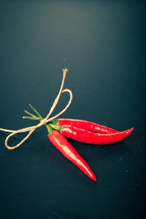 Three red hot chilli pepper with rope on old black background. Toned.の写真素材