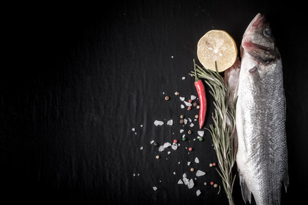 Fresh fish, lemon, pepper and rosemary on a black background. Tintedの写真素材
