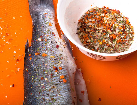 fish and spices on a plastic cutting board. Fish in the process of rubbing spices. tintedの写真素材