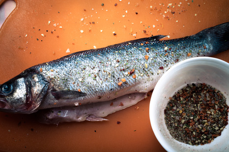 fish and spices on a plastic cutting board. Fish in the process of rubbing spices. tintedの写真素材