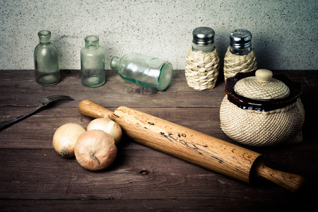 Onion, salt, pepper, rolling pin, old bottles and fork on the old wooden table. Toned.の写真素材