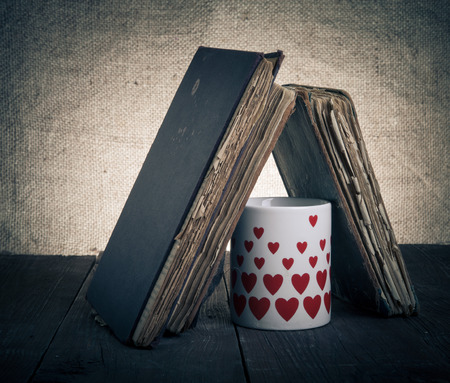 Old books and mug with many pictured hearts on the old wooden table. Toned.の写真素材