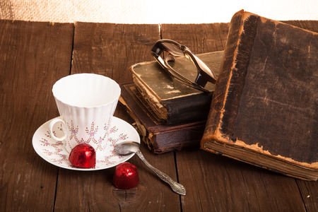 Cup of coffee, shokolad, glasses and stack of old books on the old wooden table.の写真素材