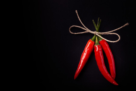 Three hot red chili pepper related by twine with on a black background. With space for text. Toned.の写真素材