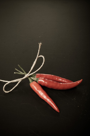 Three red hot chilli pepper with rope on old black background. Toned.の写真素材
