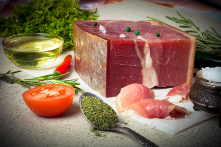 Jamon with herbs and spices, salt, olive oil and tomatoes on stone background. Toned.の写真素材