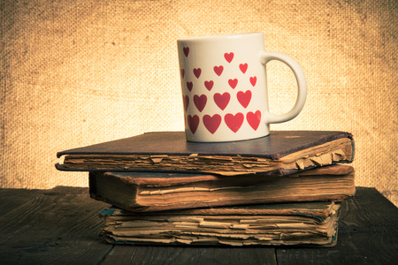 Old books and mug with many pictured hearts on the old wooden table. Toned.の写真素材