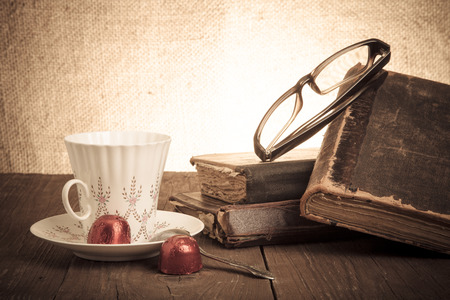 Cup of coffee, shokolad, glasses and stack of old books on the old wooden table. Toned.の写真素材