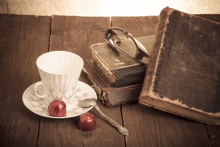 Cup of coffee, shokolad, glasses and stack of old books on the old wooden table. Toned.の写真素材