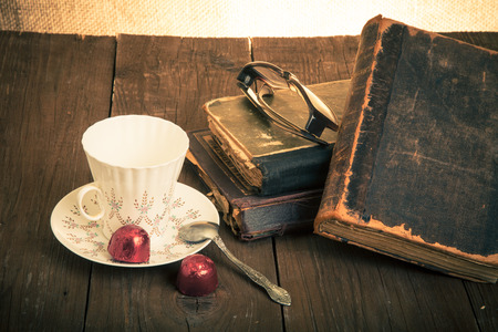 Cup of coffee, shokolad, glasses and stack of old books on the old wooden table. Toned.の写真素材