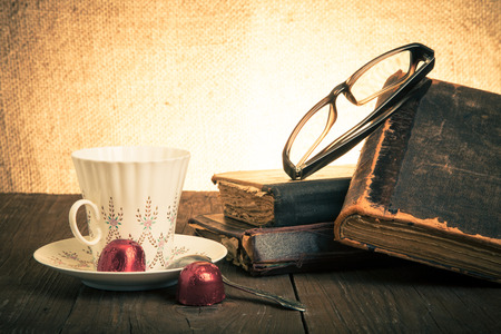 Cup of coffee, shokolad, glasses and stack of old books on the old wooden table. Toned.の写真素材
